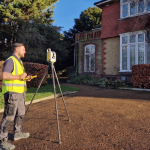 Surveyor using tripod laser scanner outside traditional house in sunlit setting